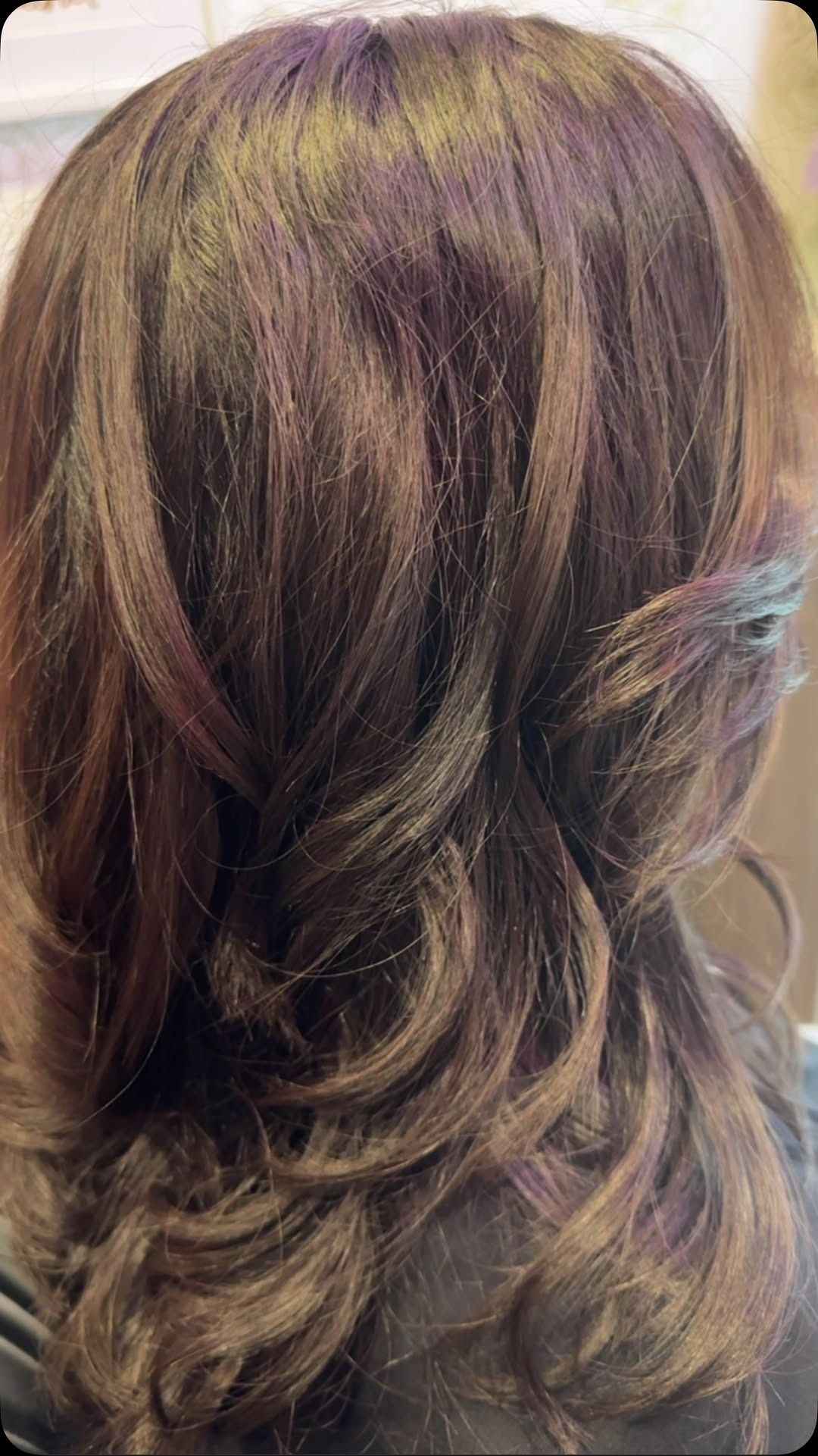 Brown wavy hair with subtle purple and teal highlights.