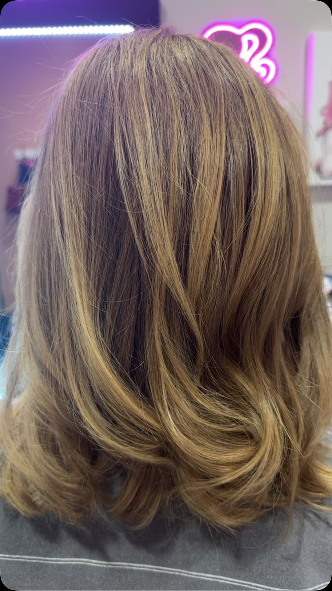 Back of a person's wavy, layered blonde and brown hair. Soft lighting in a salon setting.