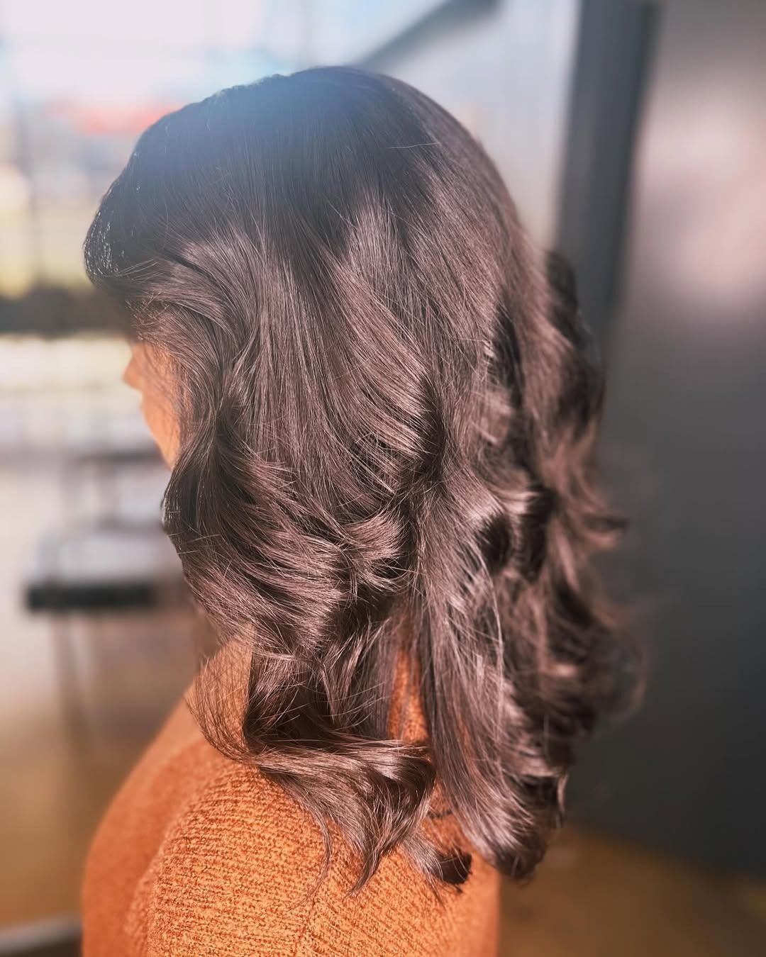 Woman with dark brown wavy hair, wearing a brown sweater, indoors.