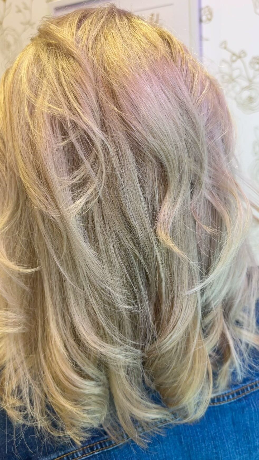 Blonde, wavy hair with pink highlights; styled indoors.