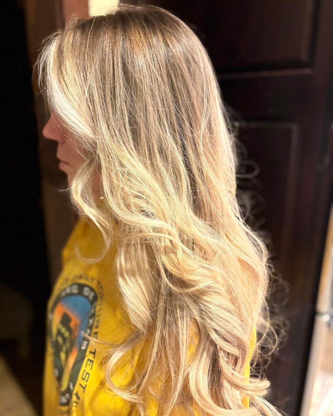 Blonde hair with highlights, styled in loose waves, worn by a person in a yellow shirt.
