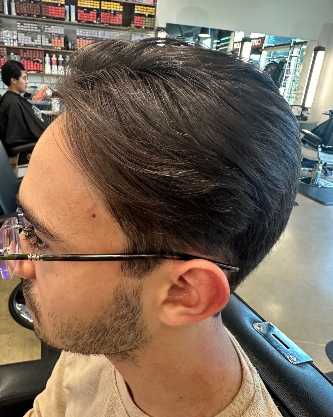 Man with dark hair and glasses in a salon chair, looking to the side.
