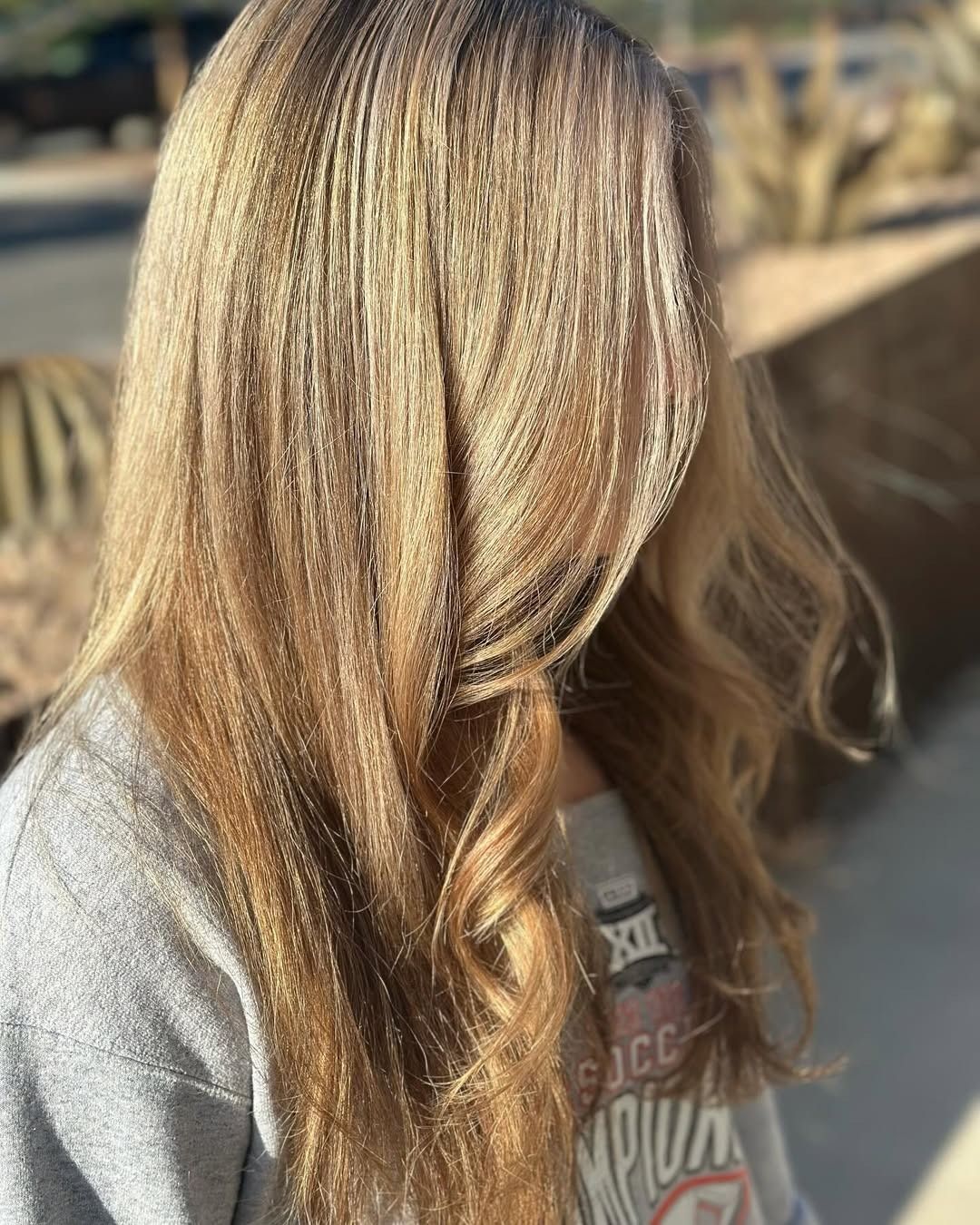 Blonde wavy hair with a gray sweatshirt outdoors.