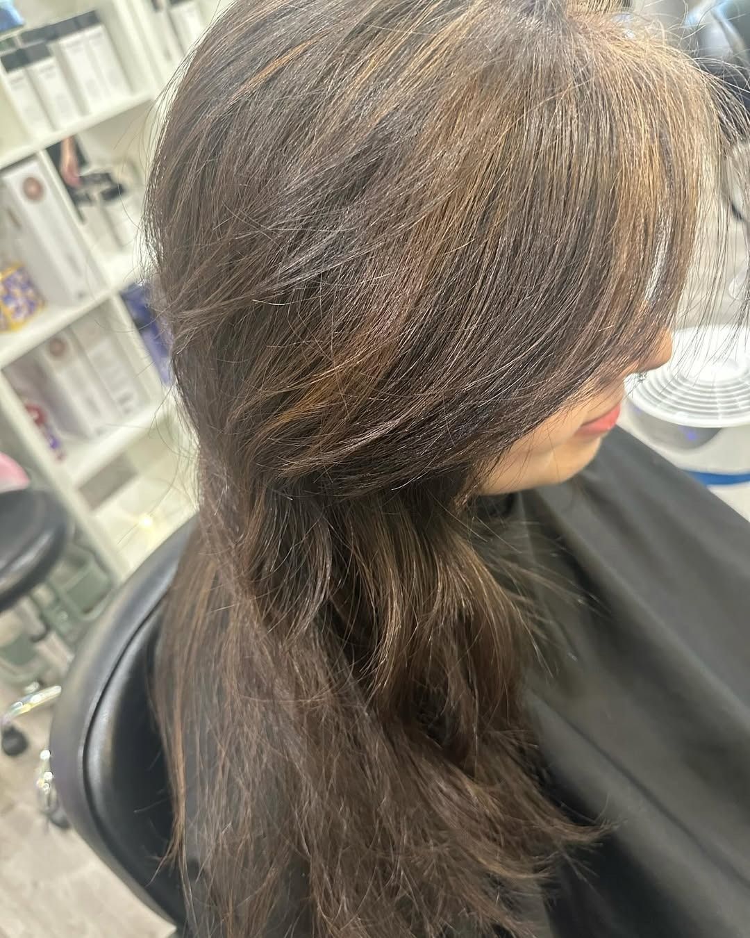 Woman with layered brown hair, some highlights, in a salon chair.
