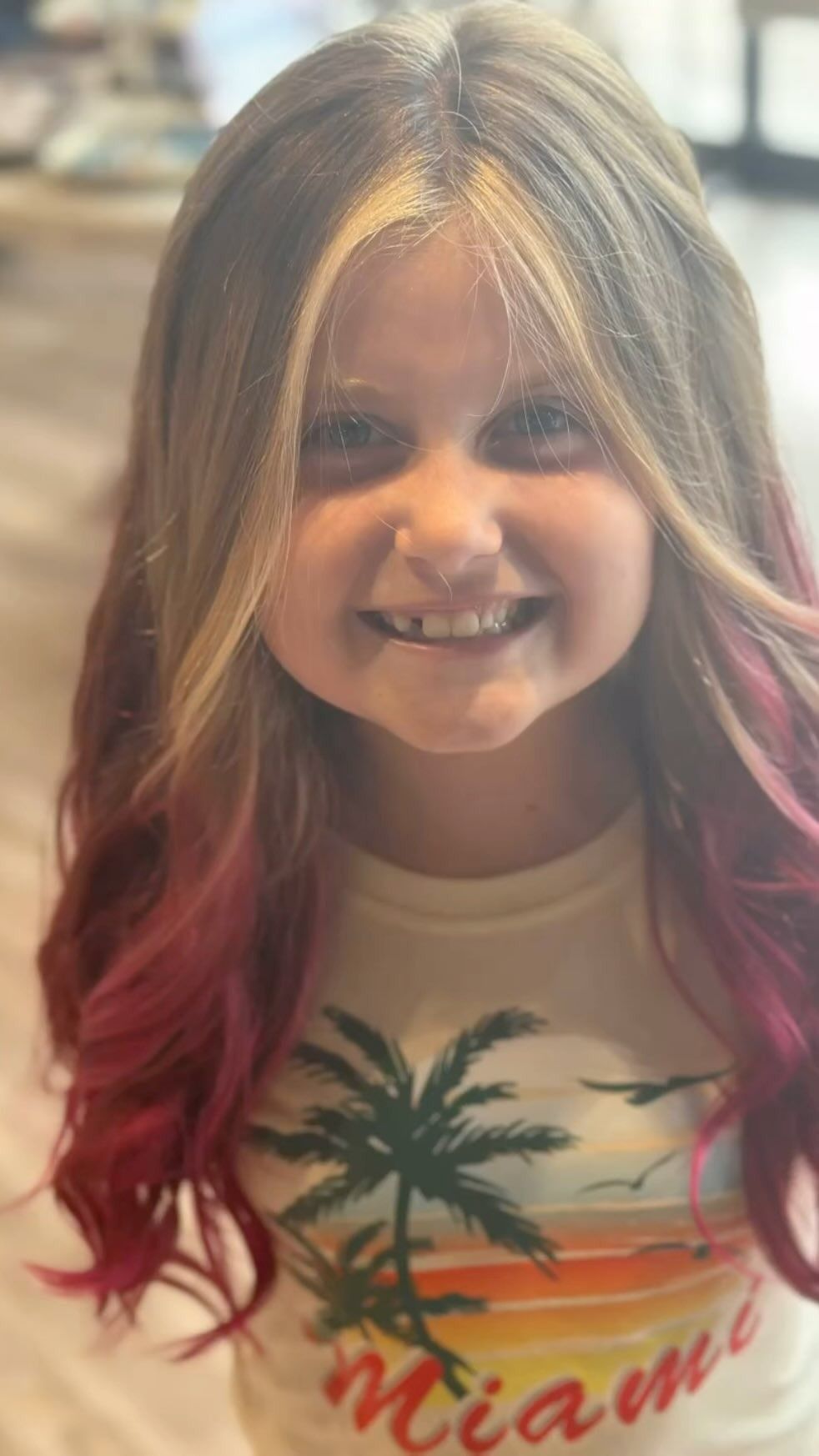 Girl with long blonde hair, pink tips, and a big smile wearing a 