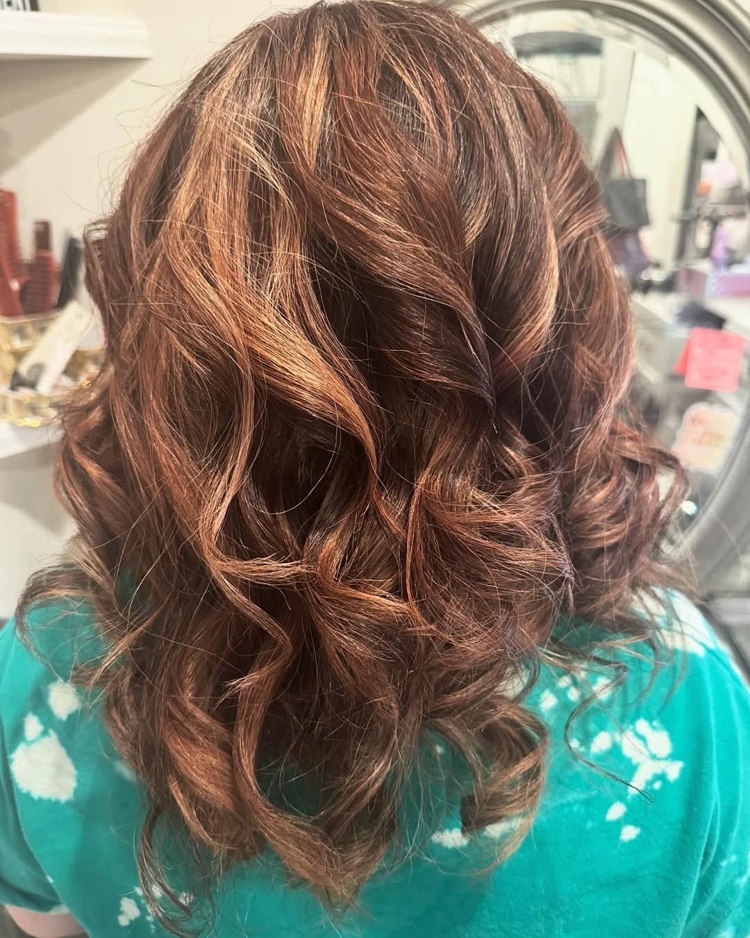 Woman with auburn hair styled in loose curls; wearing a turquoise tie-dye shirt.