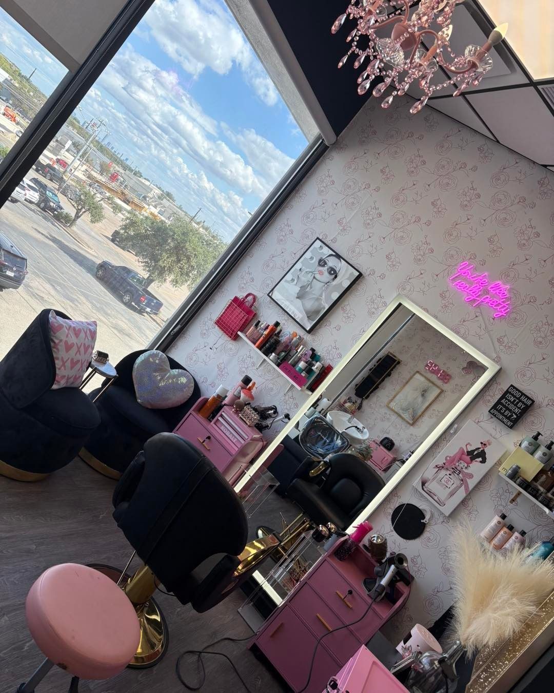 Salon interior with pink and gold accents, large mirror, and view of the outside.