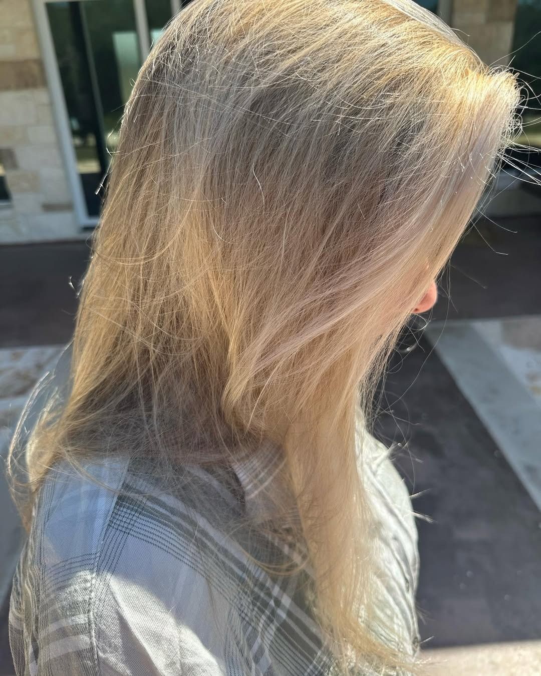 Person with light blonde hair, side view. Outdoors, wearing a plaid shirt. Sunlight highlights hair.