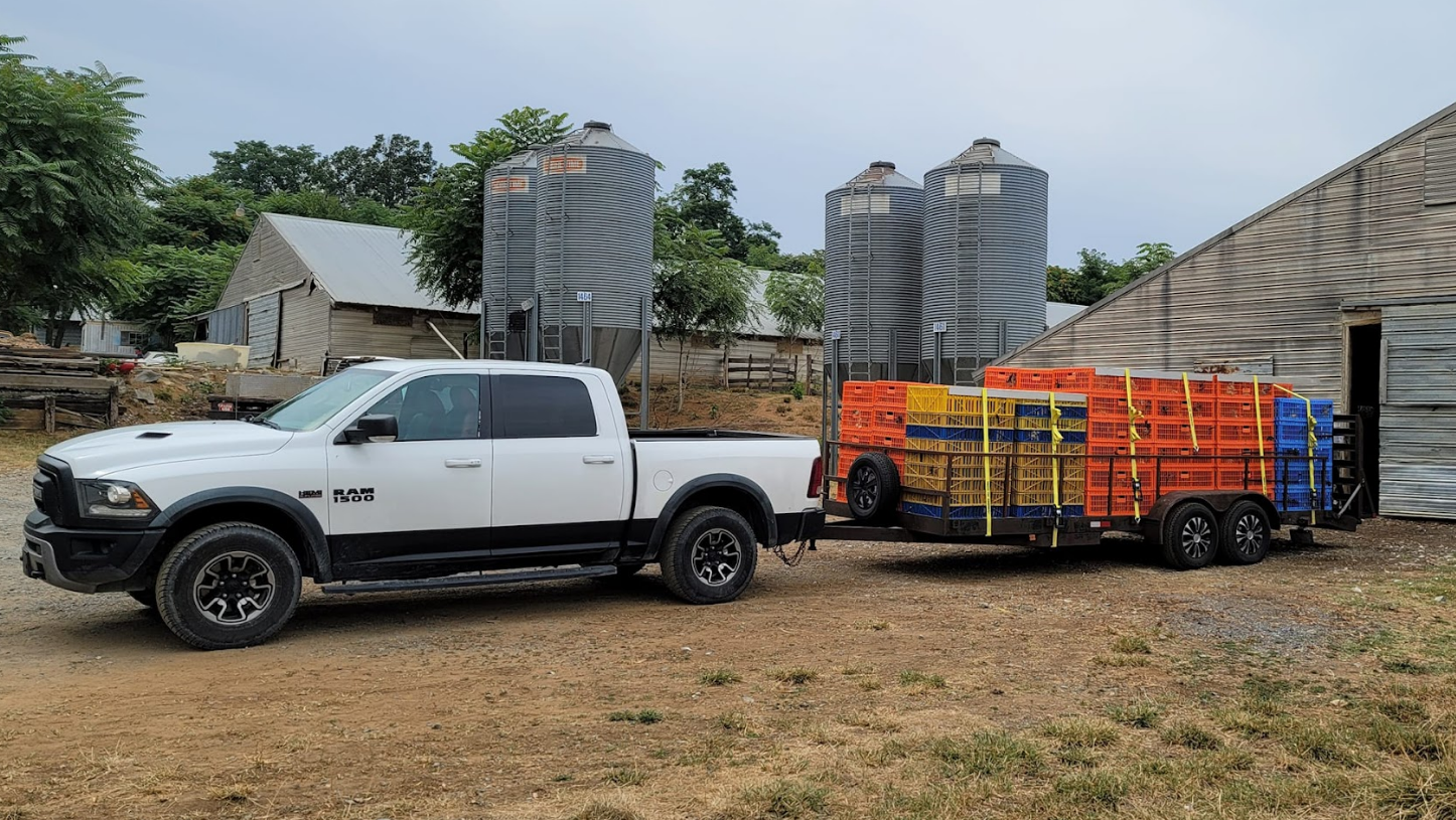 A white ram truck is pulling a trailer full of crates.