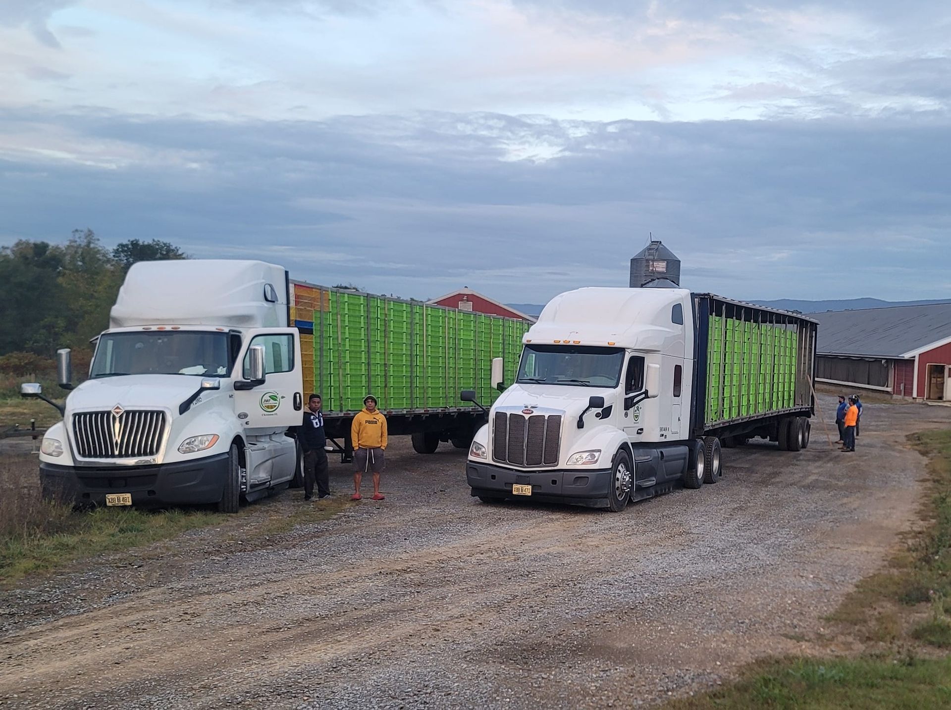 Two semi trucks are parked next to each other on a dirt road.