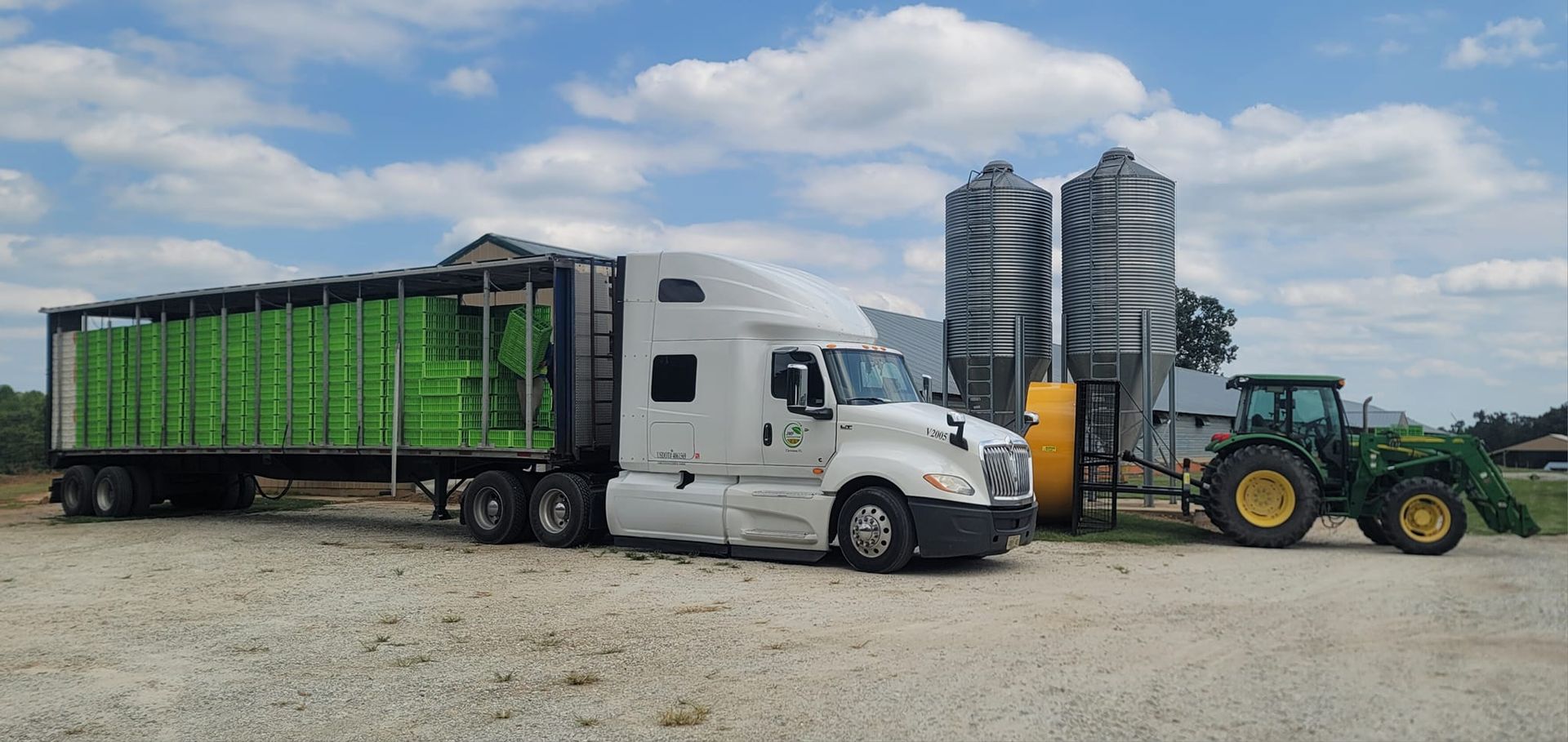 A semi truck is parked next to a tractor in a gravel lot.