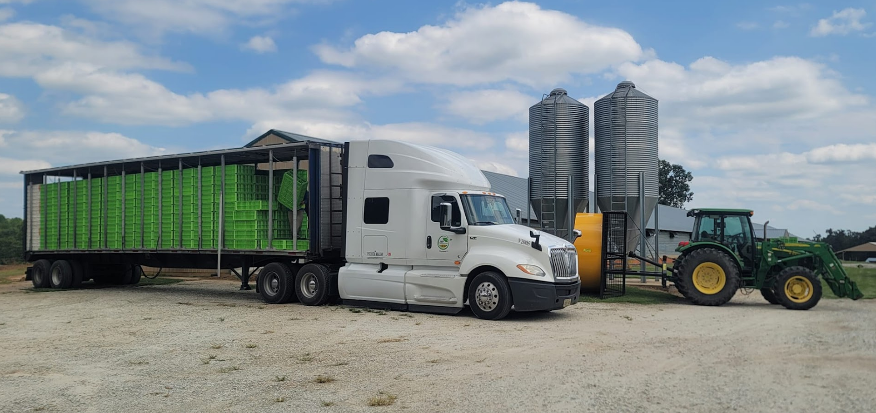 A semi truck is parked in a gravel lot next to a tractor.