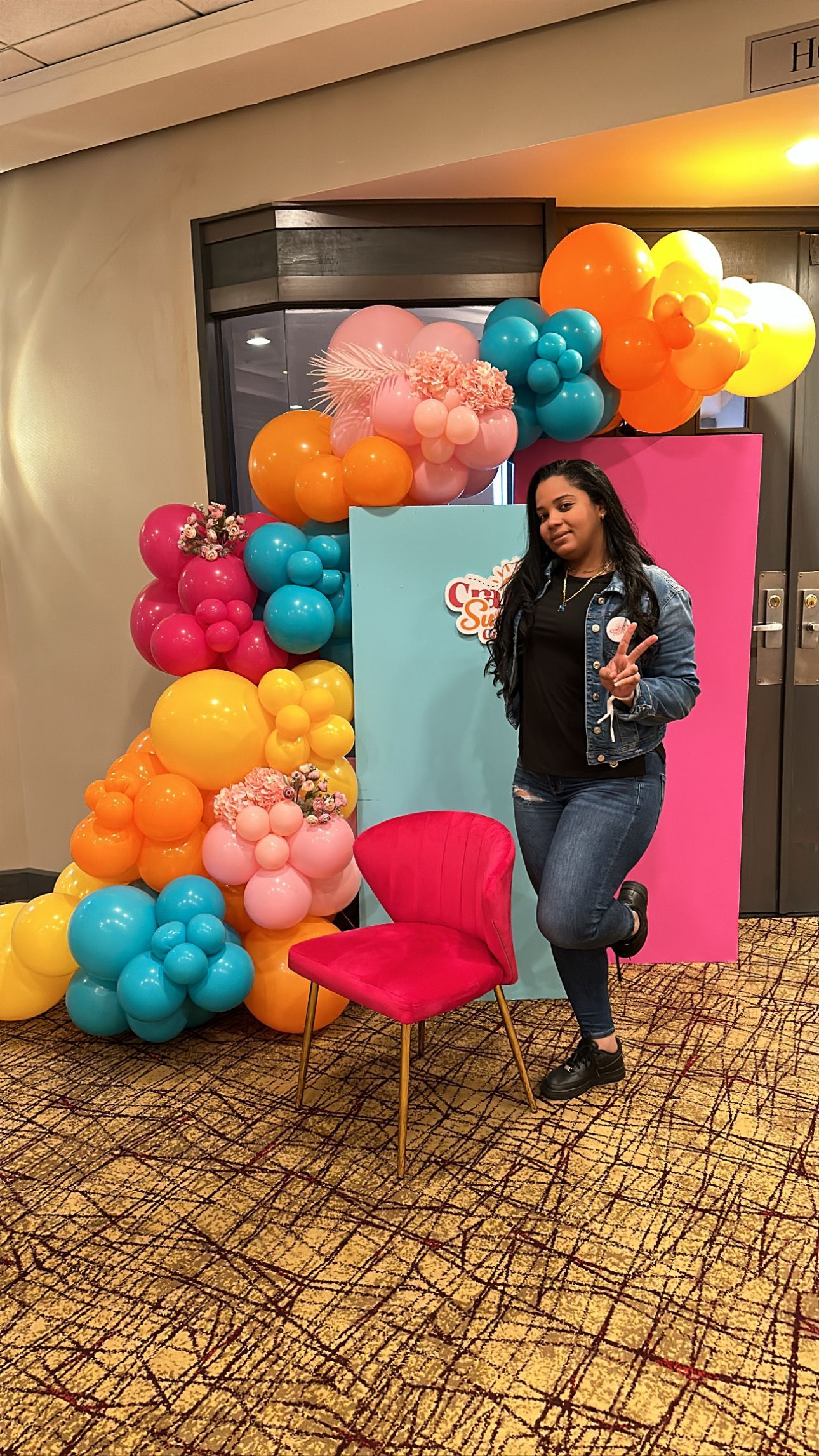 A woman is standing in front of a wall of balloons.