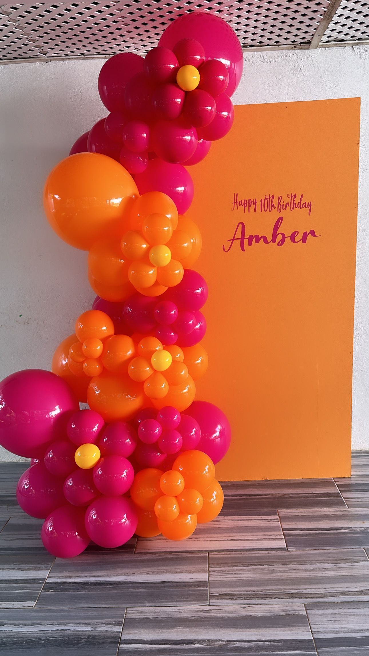 A bunch of pink and orange balloons are hanging on a wall.
