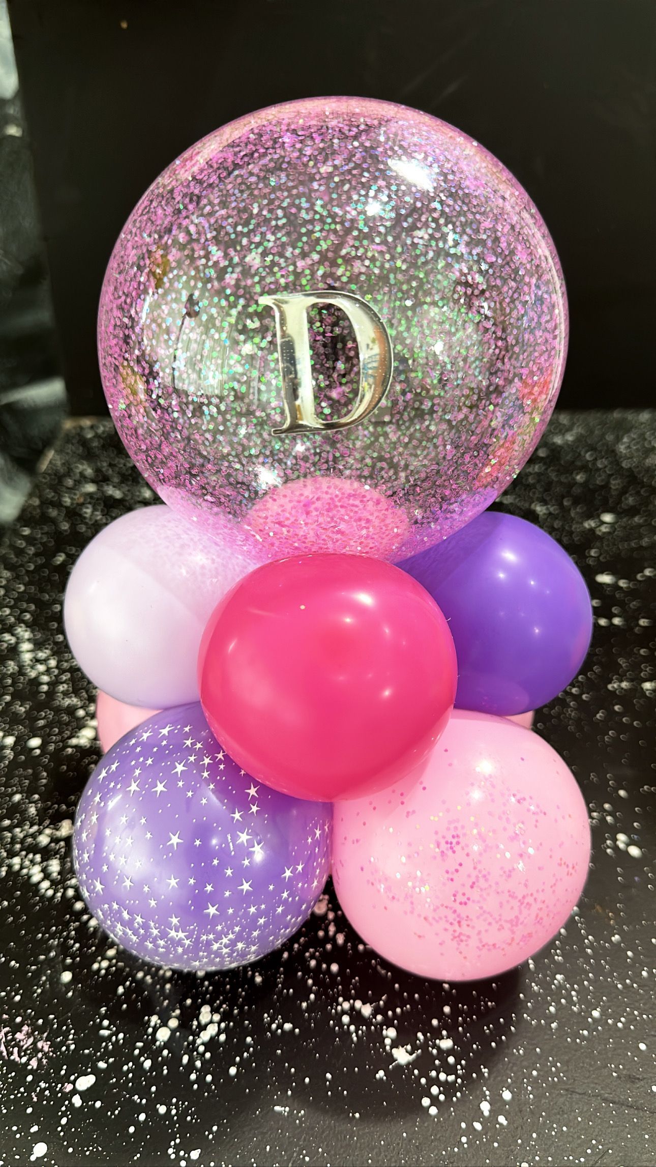 A pink balloon with a letter d on it is surrounded by pink and purple balloons.