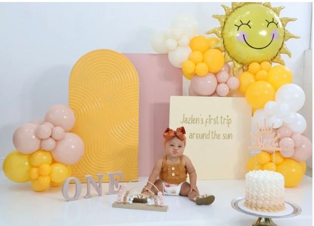 A baby is sitting in front of balloons and a sign that says one