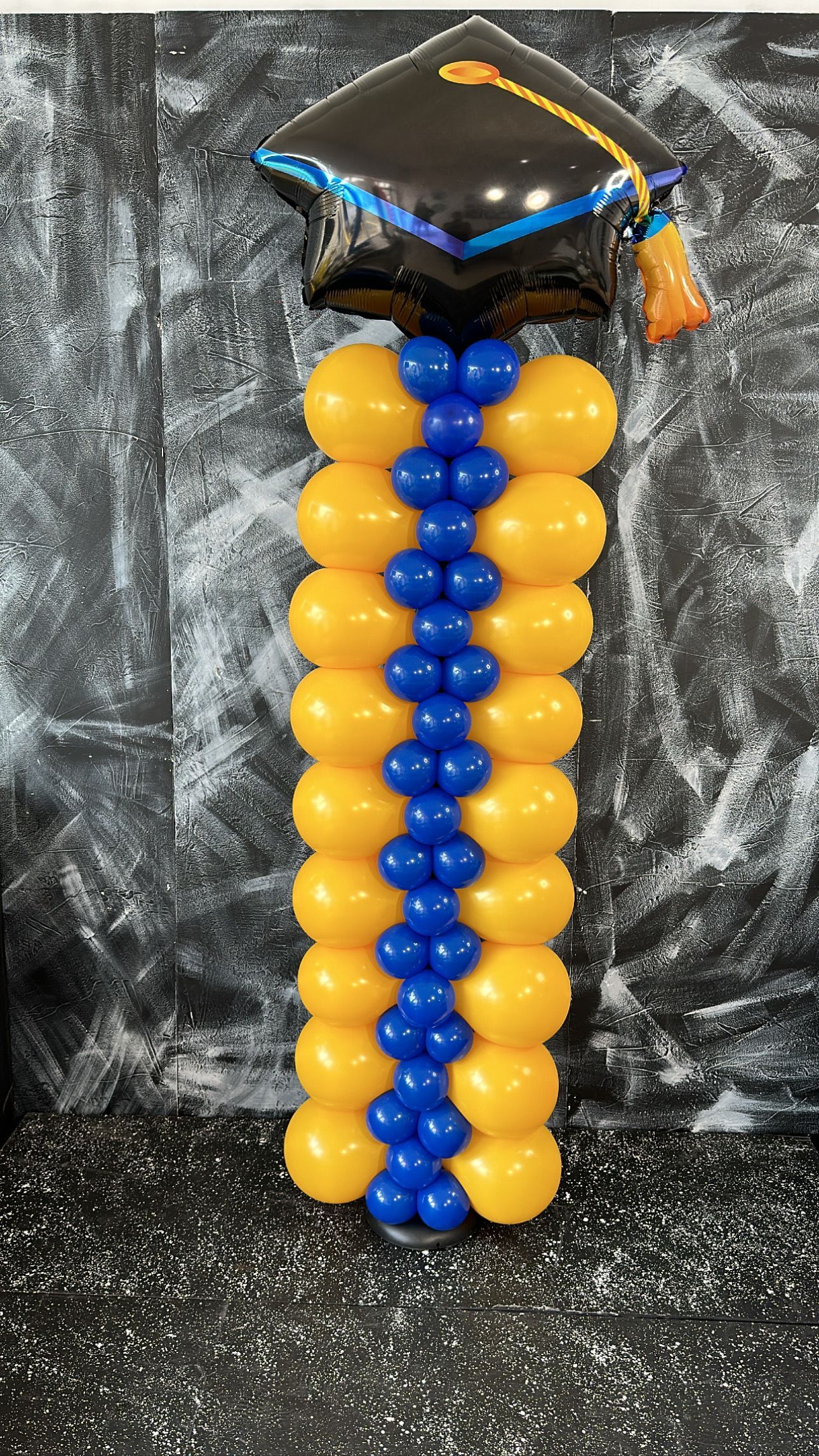 A blue and yellow balloon column with a graduation cap on top of it.