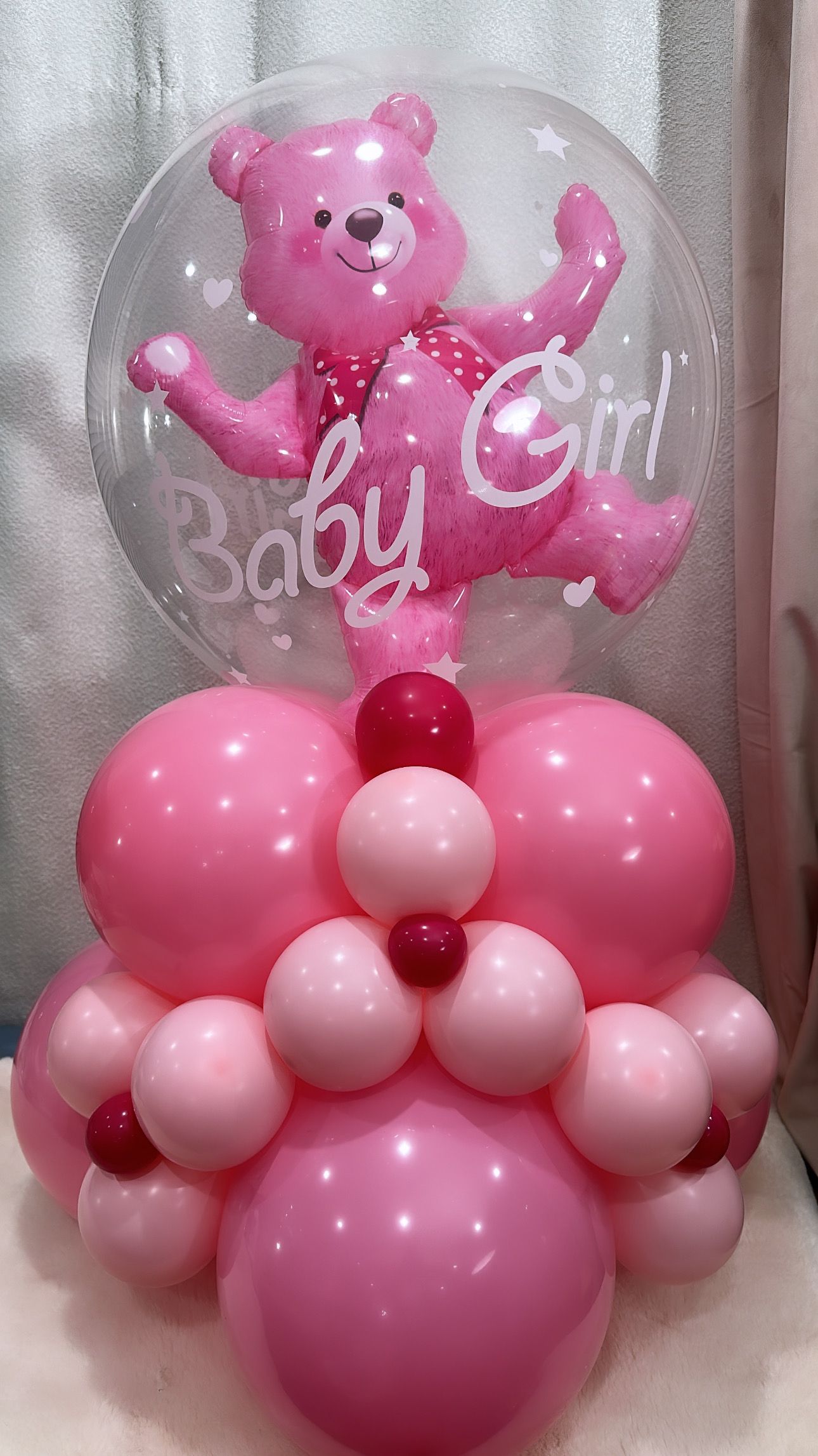 A pink teddy bear is sitting inside of a baby girl balloon.