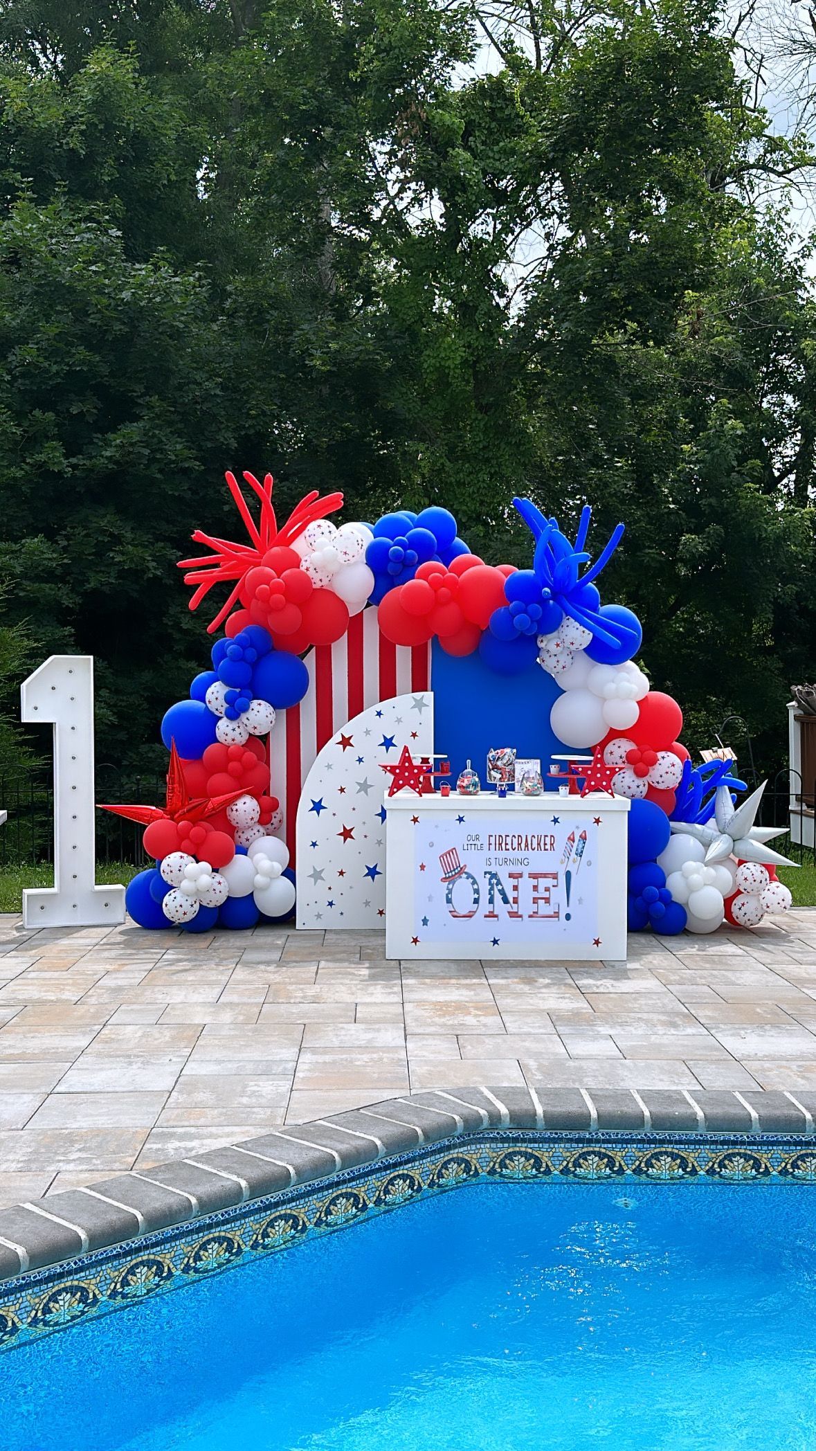 A table decorated with red , white and blue balloons next to a pool.