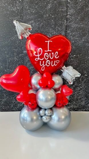 A red heart with the words `` i love you '' written on it is surrounded by silver balloons.