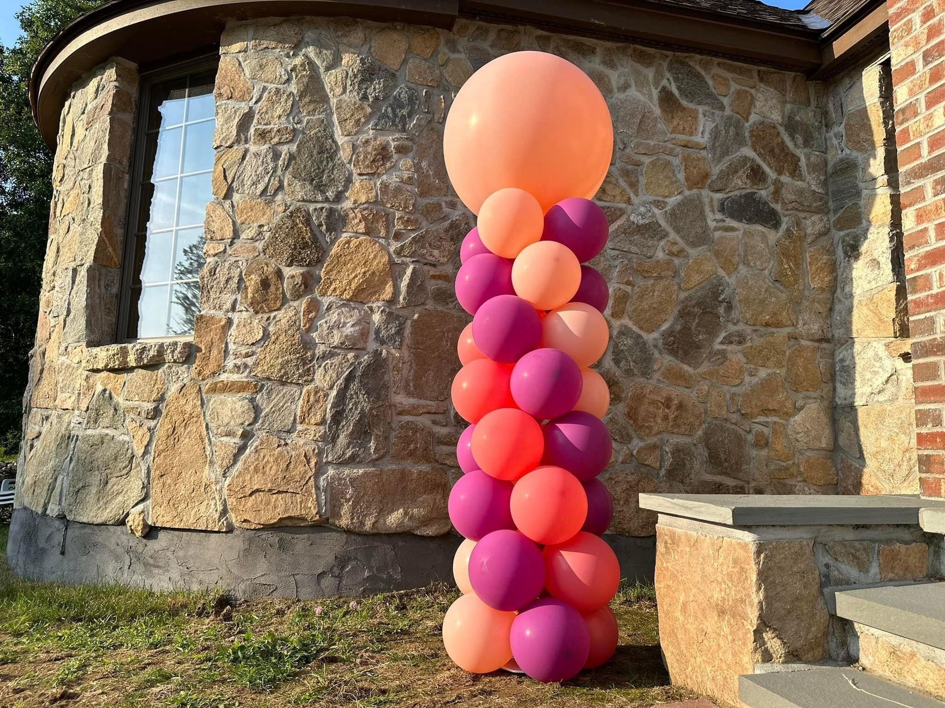 A woman is standing next to a hot air balloon made of pink and gold balloons.