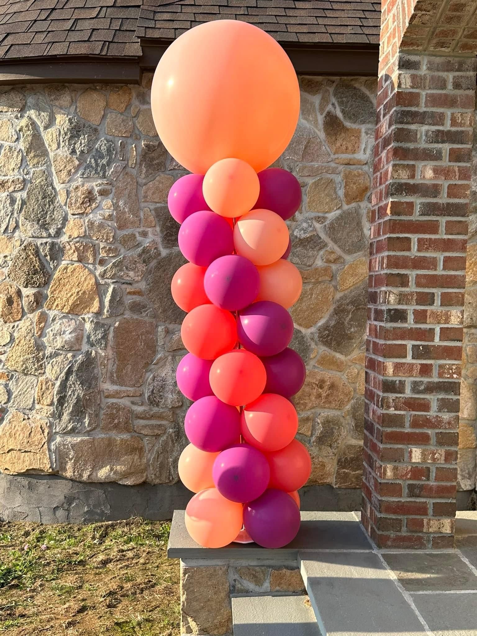 A bunch of balloons are stacked on top of each other in front of a brick building. balloon columns