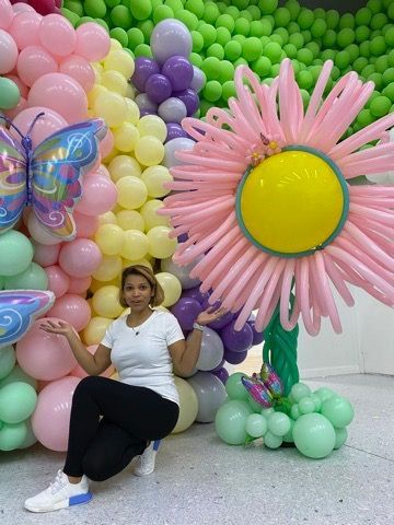 A woman is kneeling in front of a wall of balloons.