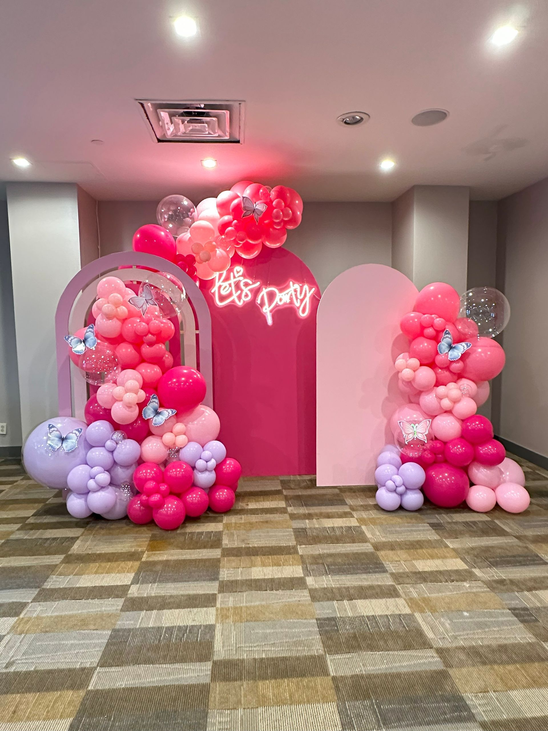 A room filled with pink and purple balloons and a neon sign.