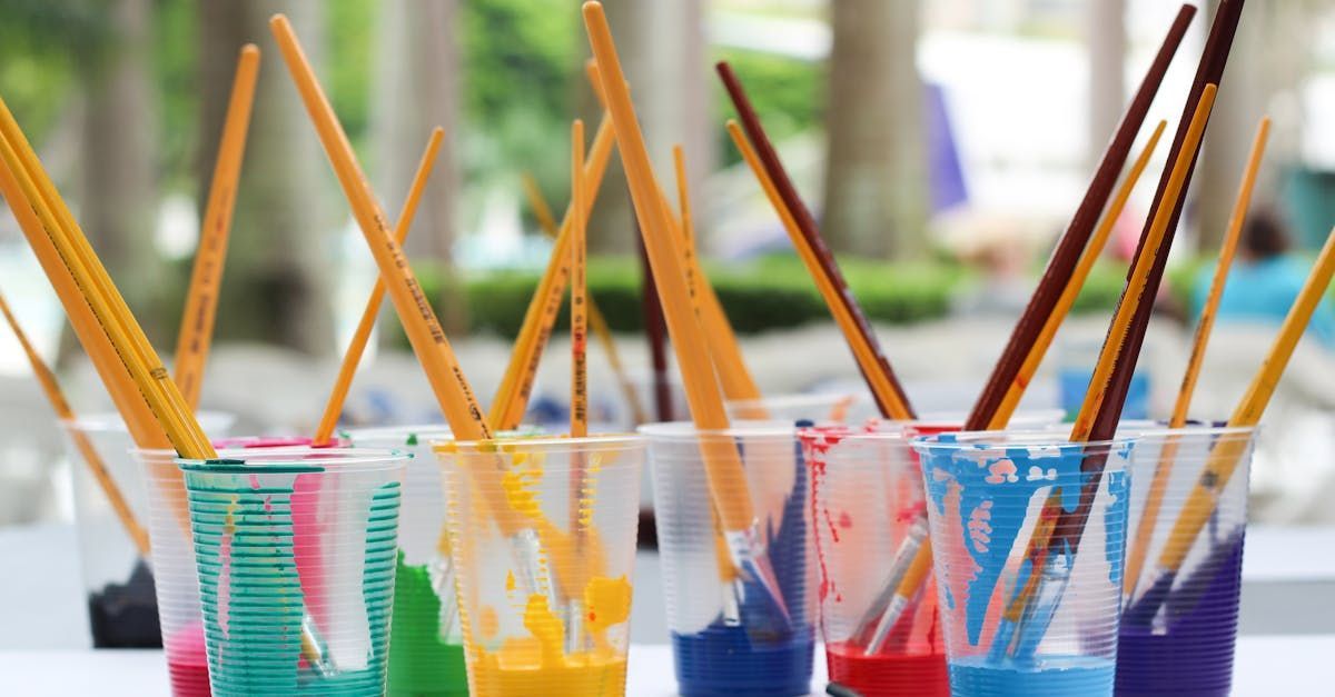 A row of plastic cups filled with different colored paint and brushes.