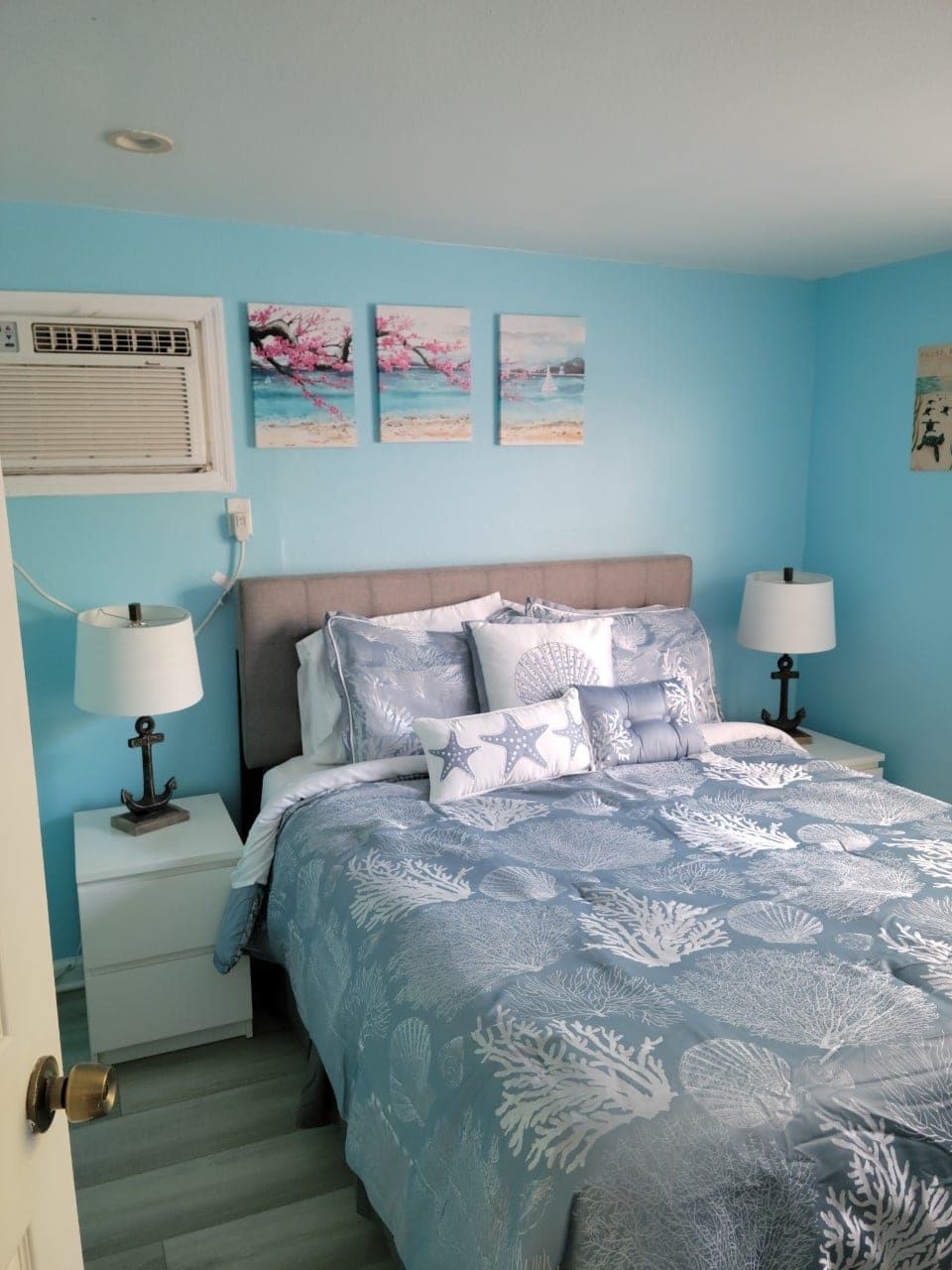 A bedroom with a bed , nightstand , lamps and paintings on the wall.