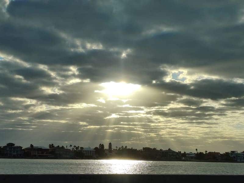 The sun is shining through the clouds over a body of water