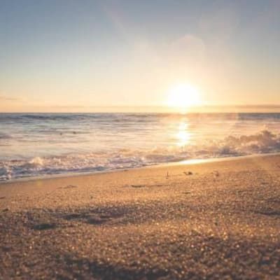 The sun is setting over the ocean on a sandy beach.
