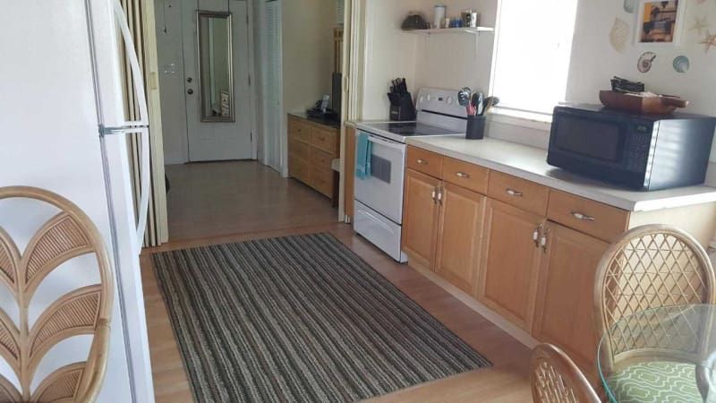 A kitchen with a stove , refrigerator , microwave and wicker chairs.