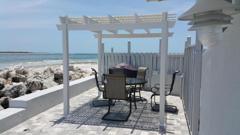 A patio with a table and chairs under a pergola overlooking the ocean.
