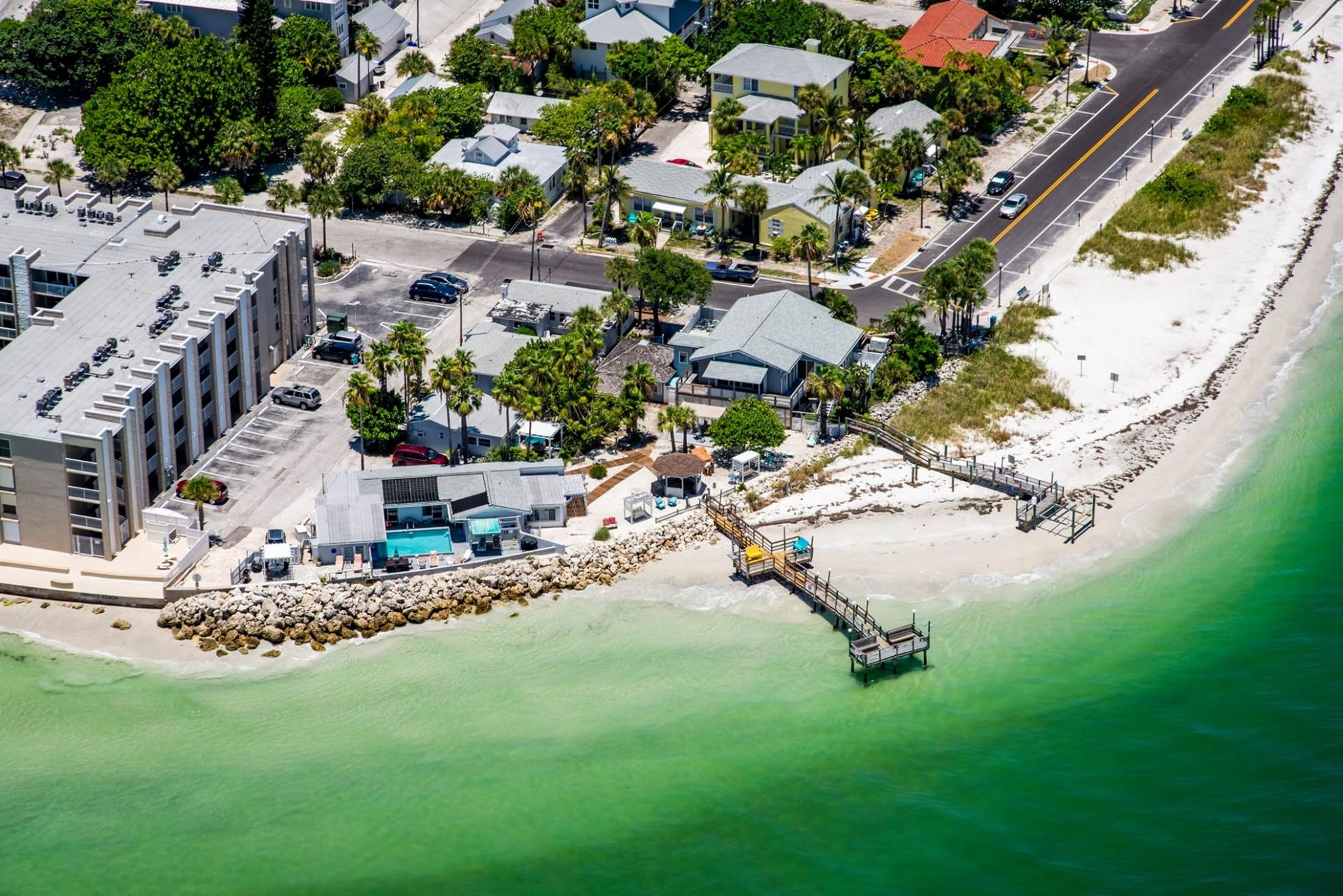 An aerial view of a beach with a dock and buildings on the shore.