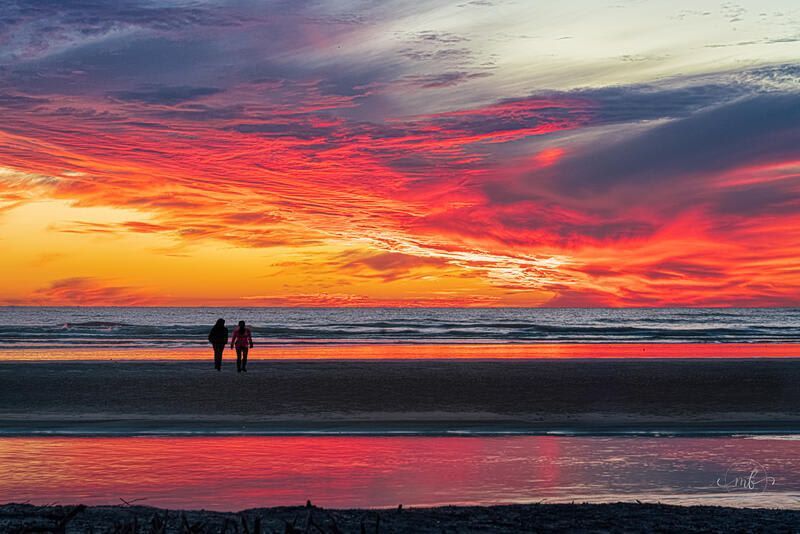 Two people are walking on the beach at sunset.