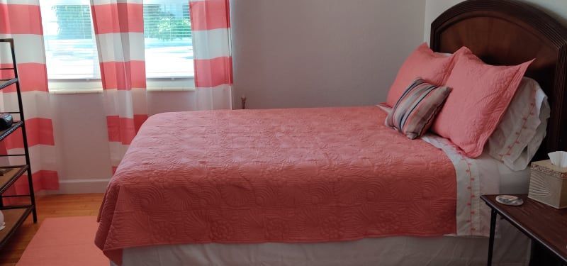 A bedroom with a bed , nightstand , and window with pink curtains.