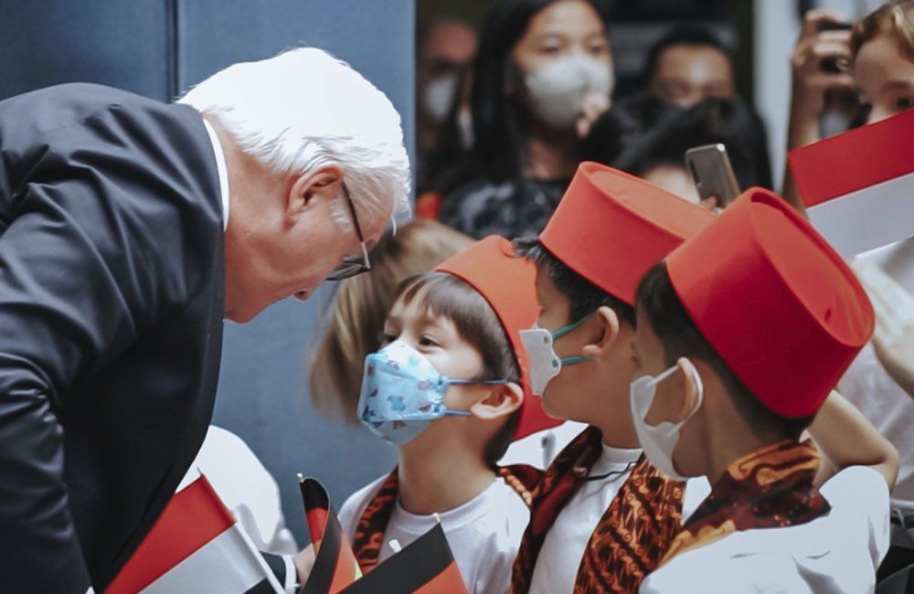 A man in a suit is talking to a group of children wearing masks.