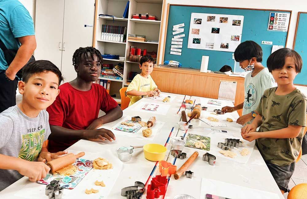 A group of children are sitting at a table in a classroom making cookies.