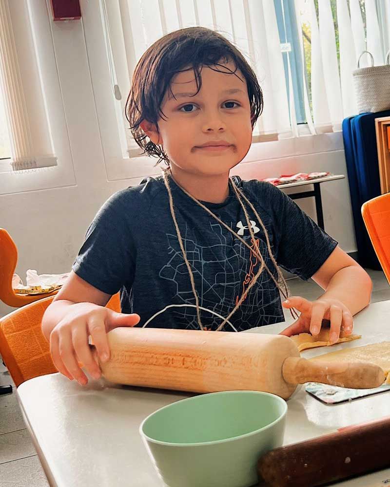 A young boy is sitting at a table holding a rolling pin