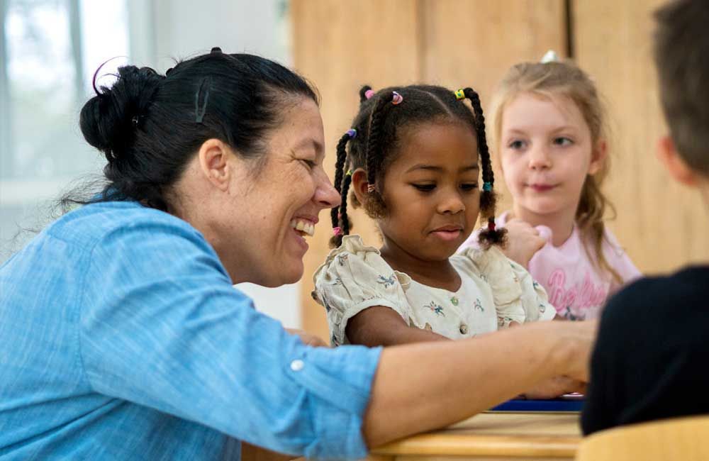 A woman is sitting at a table with a group of children.