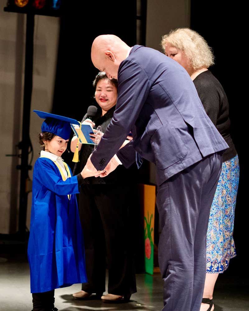 A little girl in a graduation cap and gown is being congratulated by a man in a suit