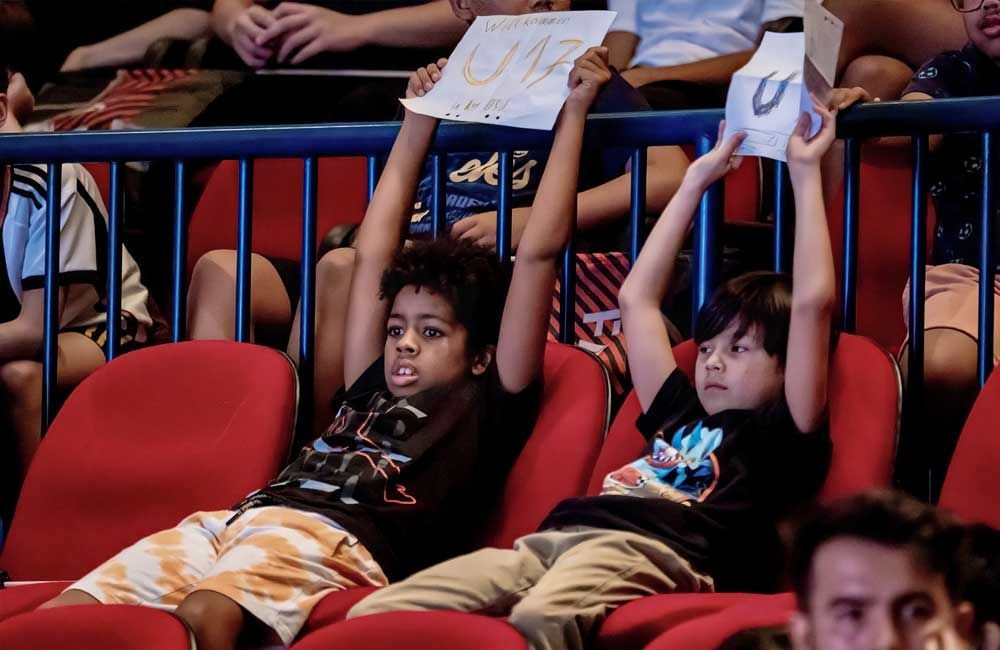 Two young boys are sitting in a stadium holding up signs.