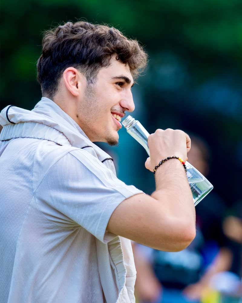 A young man is drinking water from a clear bottle.