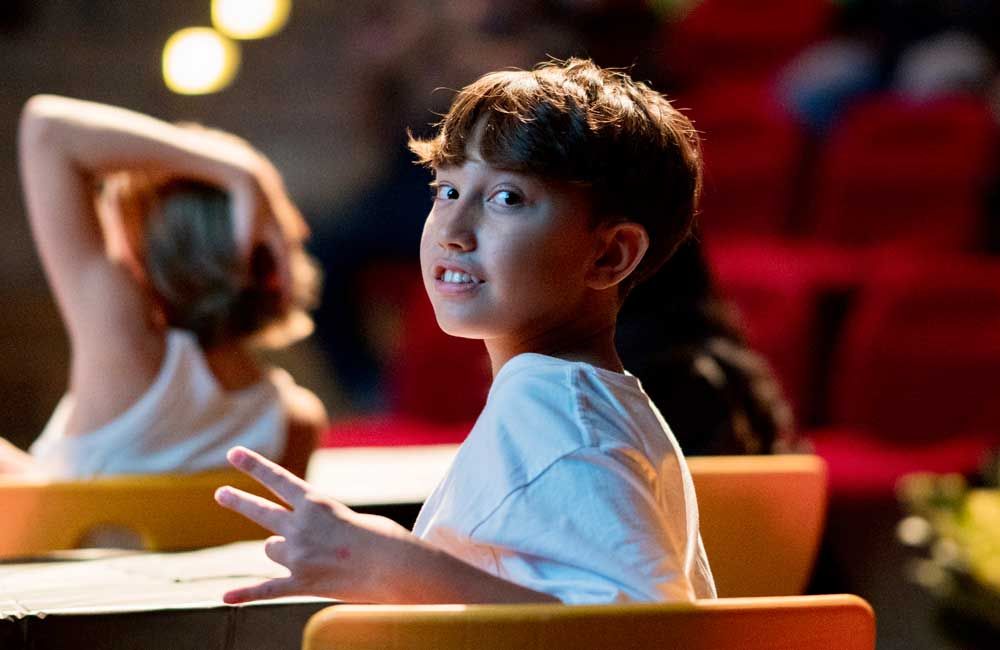 A young boy is sitting in a chair and making a peace sign.