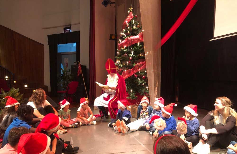 A group of children are sitting on the floor in front of a christmas tree