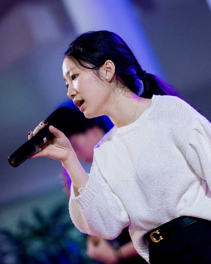 A woman in a white sweater is singing into a microphone.