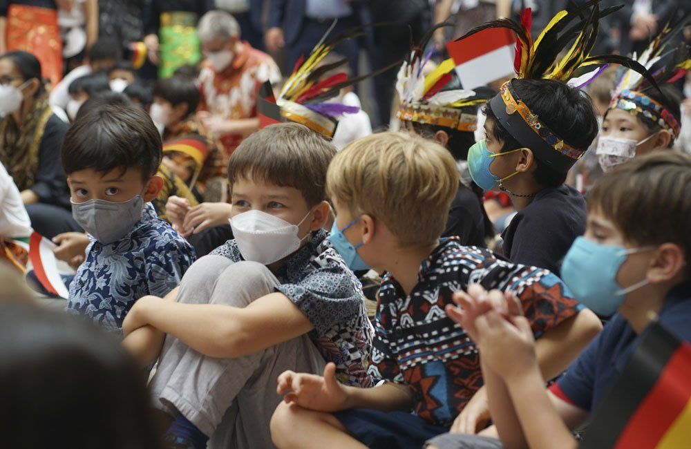 A group of children wearing face masks are sitting in a crowd.