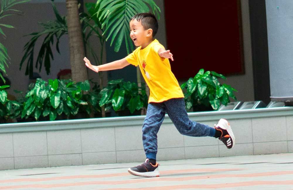 A young boy in a yellow shirt is running on a sidewalk.