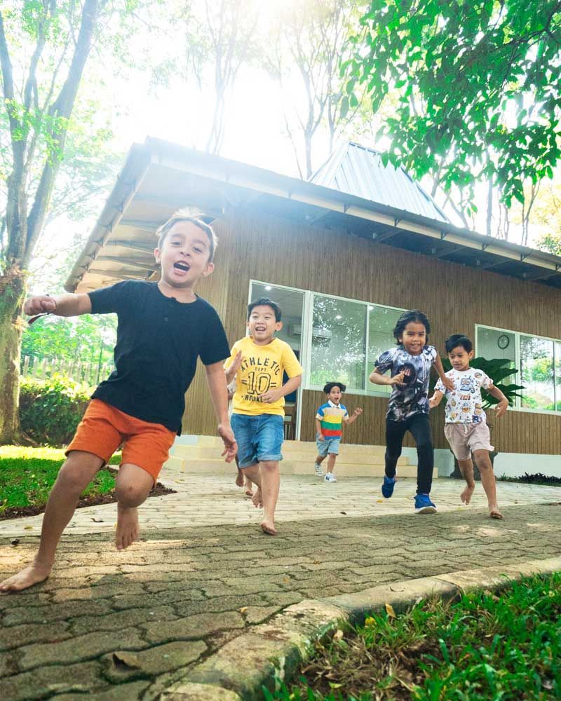 A group of children are running barefoot on a sidewalk in front of a house.